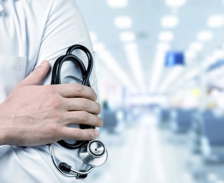 A doctor holding a stethoscope in a bright hospital corridor
