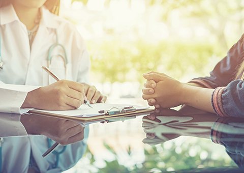 A doctor taking notes while talking with a patient